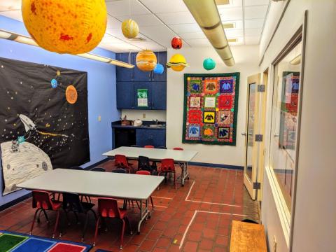 Room with tables and chairs with planets hanging from ceiling.